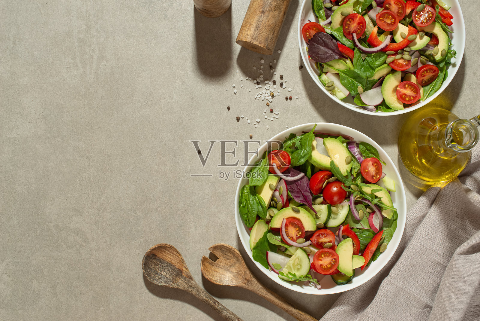 新鲜的绿色沙拉，有西红柿、黄瓜、萝卜、甜椒和鳄梨，装在白色盘子里，背景是灰色的。照片摄影图片