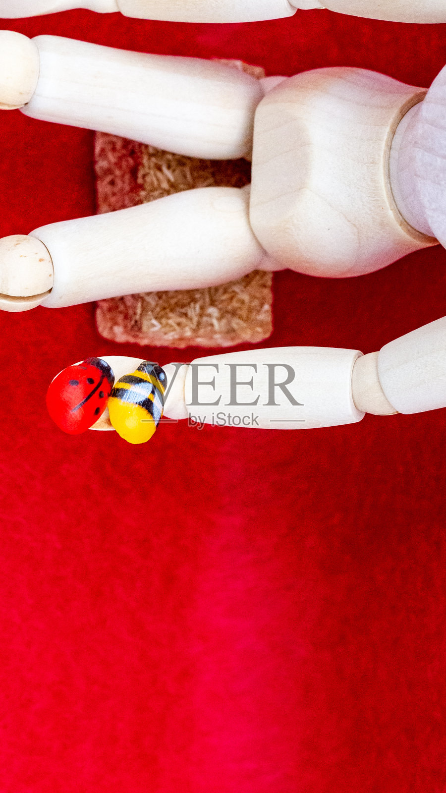 手持瓢虫和蜜蜂的木制人物，红色背景照片摄影图片