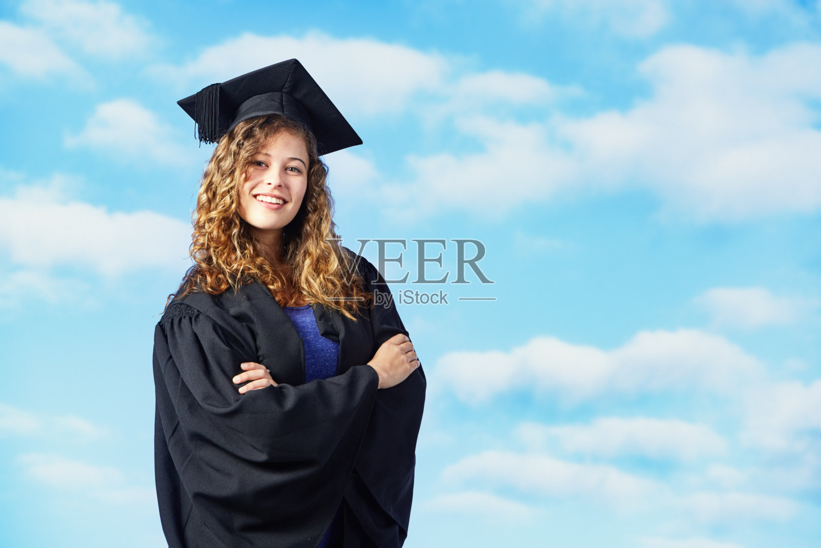美丽快乐的年轻女子穿着毕业礼服和学位帽，映衬着明亮的夏日天空照片摄影图片