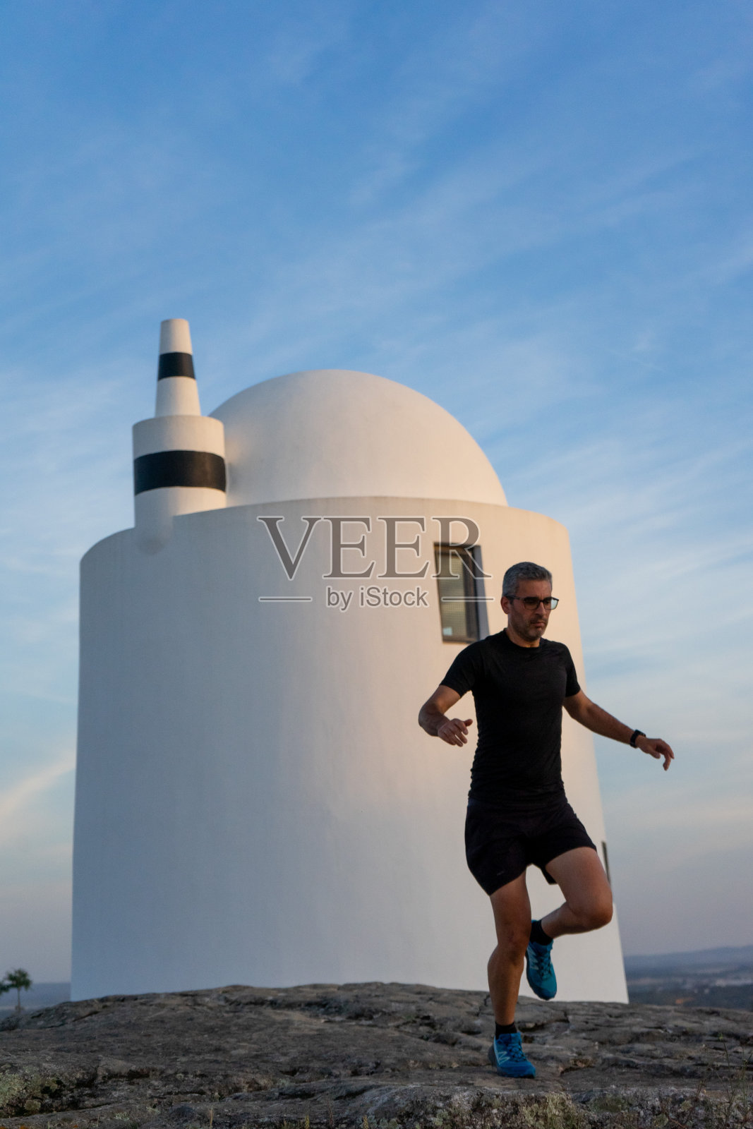 一个花白头发的男人在风车旁边跑越野跑和跳跃。照片摄影图片