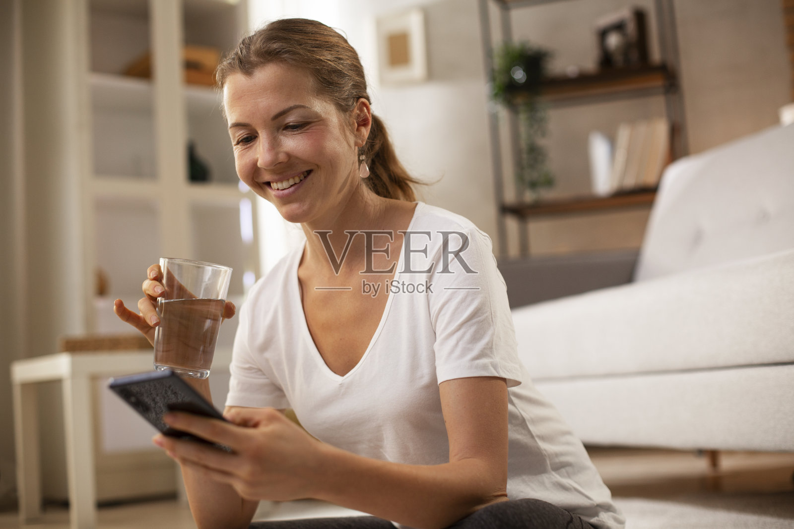 美丽的女人一边在家玩手机一边享受。照片摄影图片