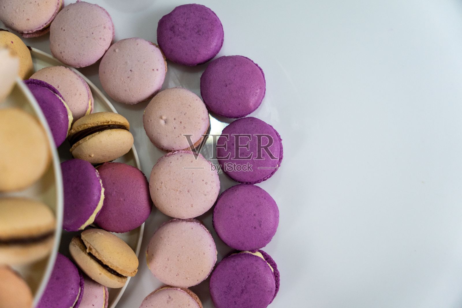 白色盘子里装着五颜六色的马卡龙，有粉色、紫色和黄色照片摄影图片