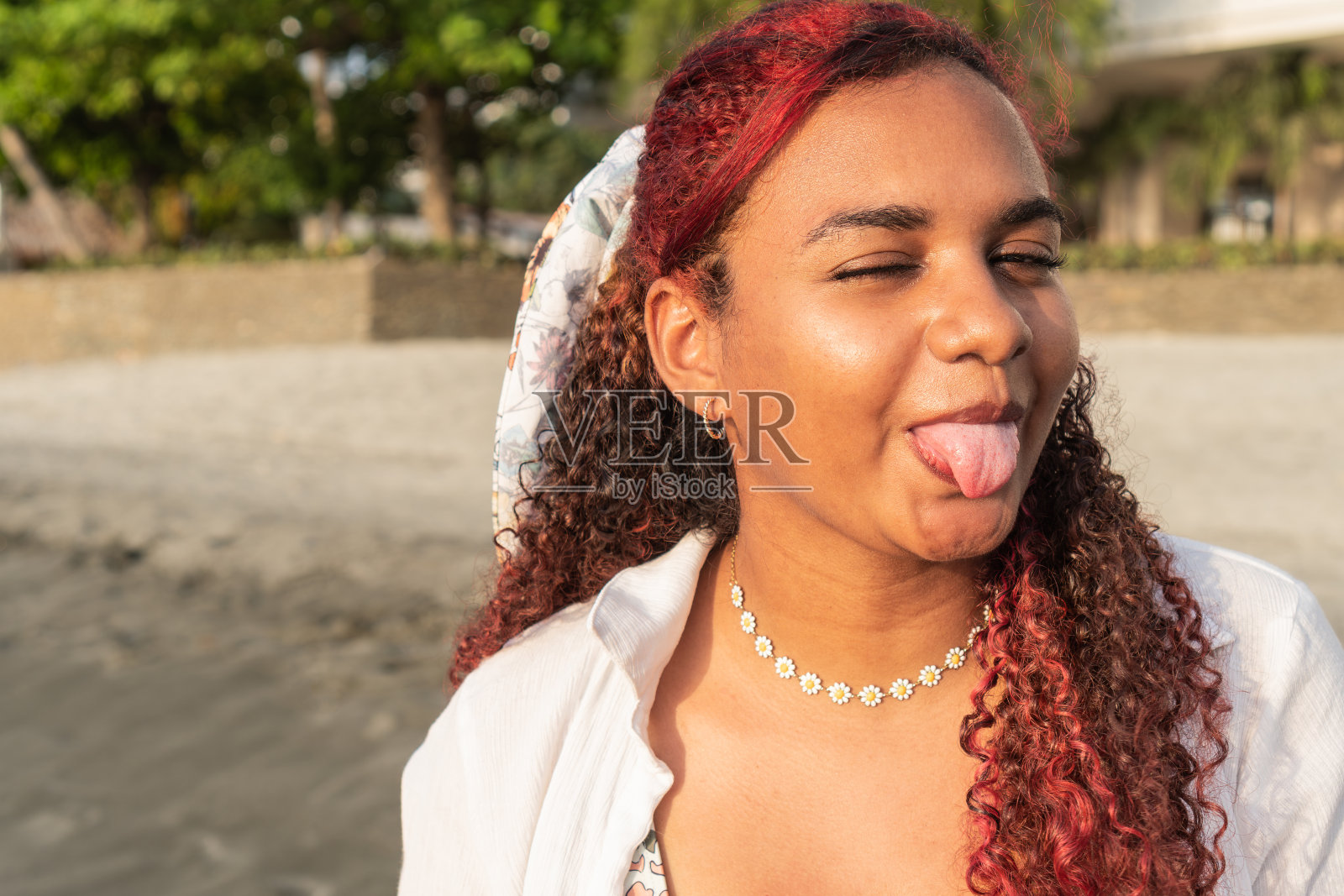 一个年轻的卷发女子在户外的画像，她伸出舌头。照片摄影图片