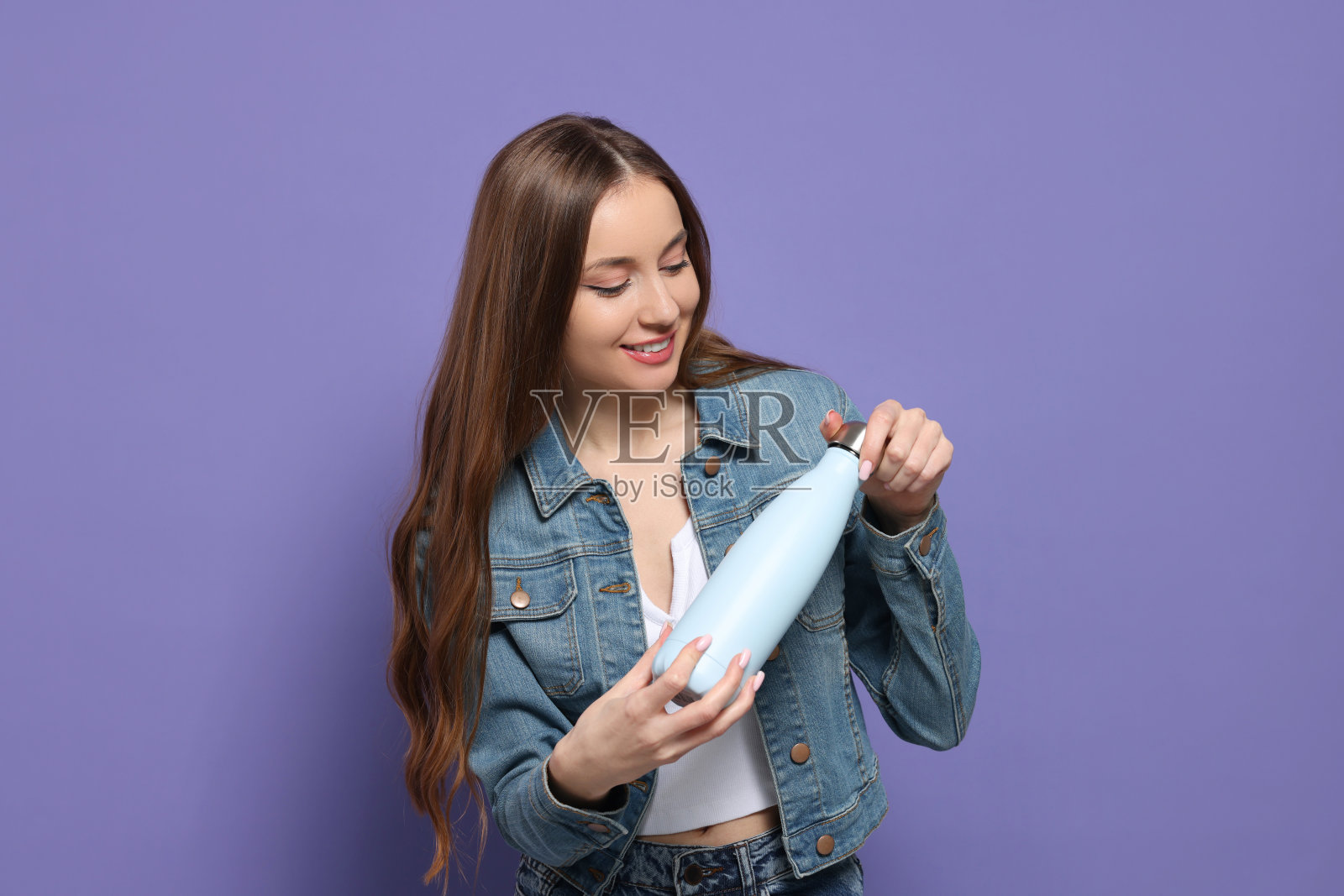 漂亮的年轻女子拿着紫色背景的保温瓶照片摄影图片