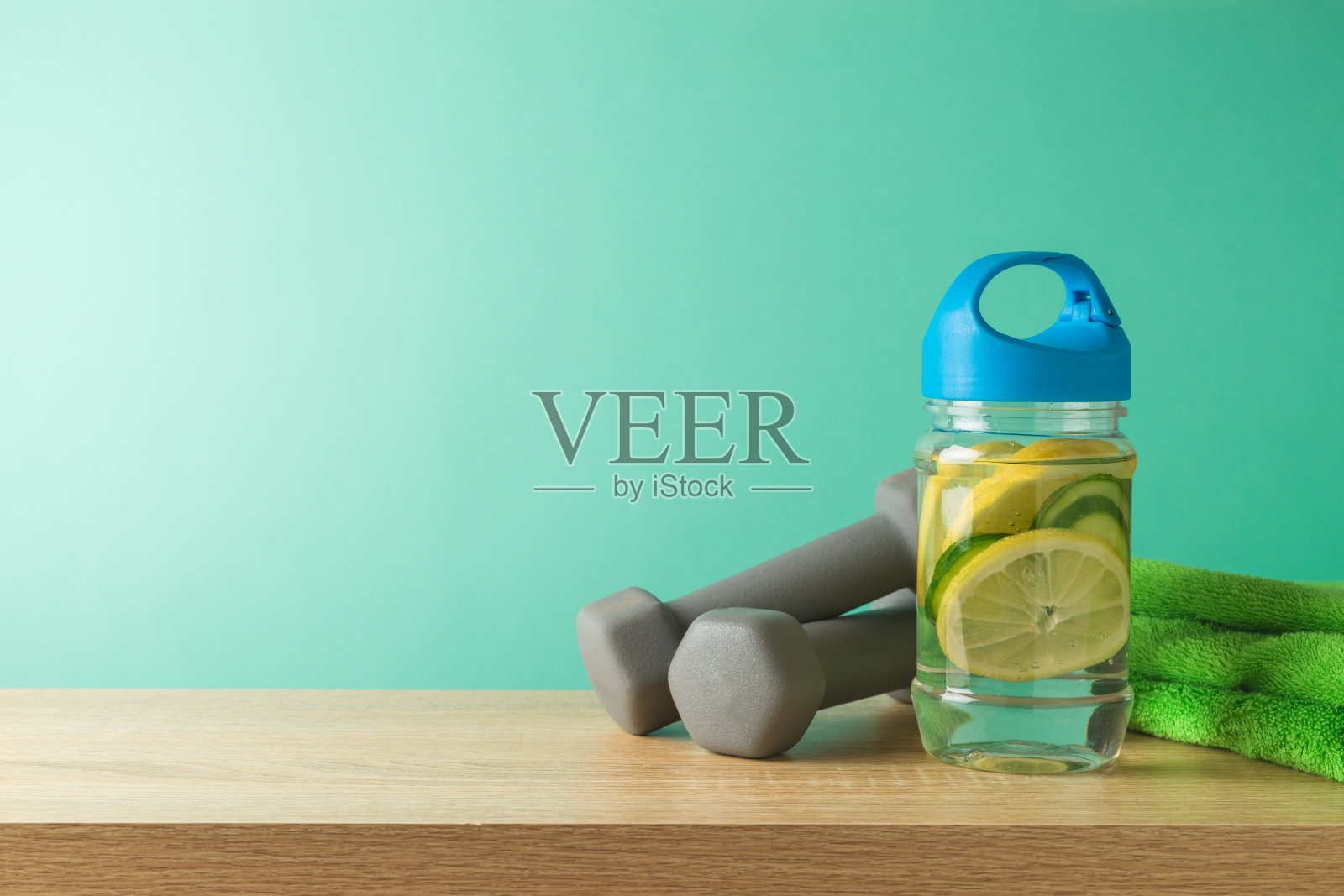 健身背景与注入柠檬和黄瓜水，毛巾和哑铃在木桌上照片摄影图片