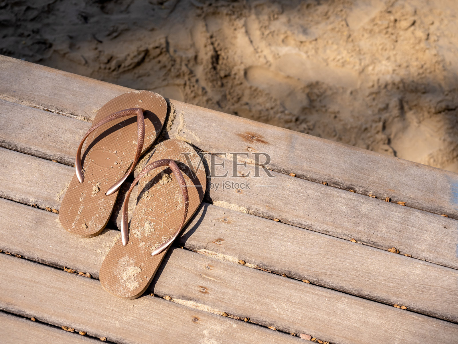 空沙沾污的女子凉鞋被脱下，在木甲板的露台上，走到沙滩上散步，夕阳下，有copy的空间。暑假、假日周末到海边旅游的概念。照片摄影图片