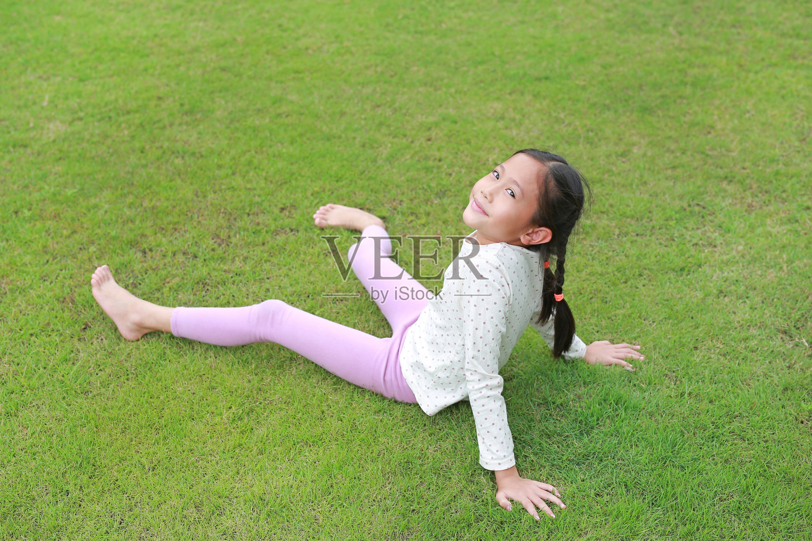 微笑的亚洲小女孩躺在花园的绿色草坪上。小孩躺在草地上看着相机。照片摄影图片