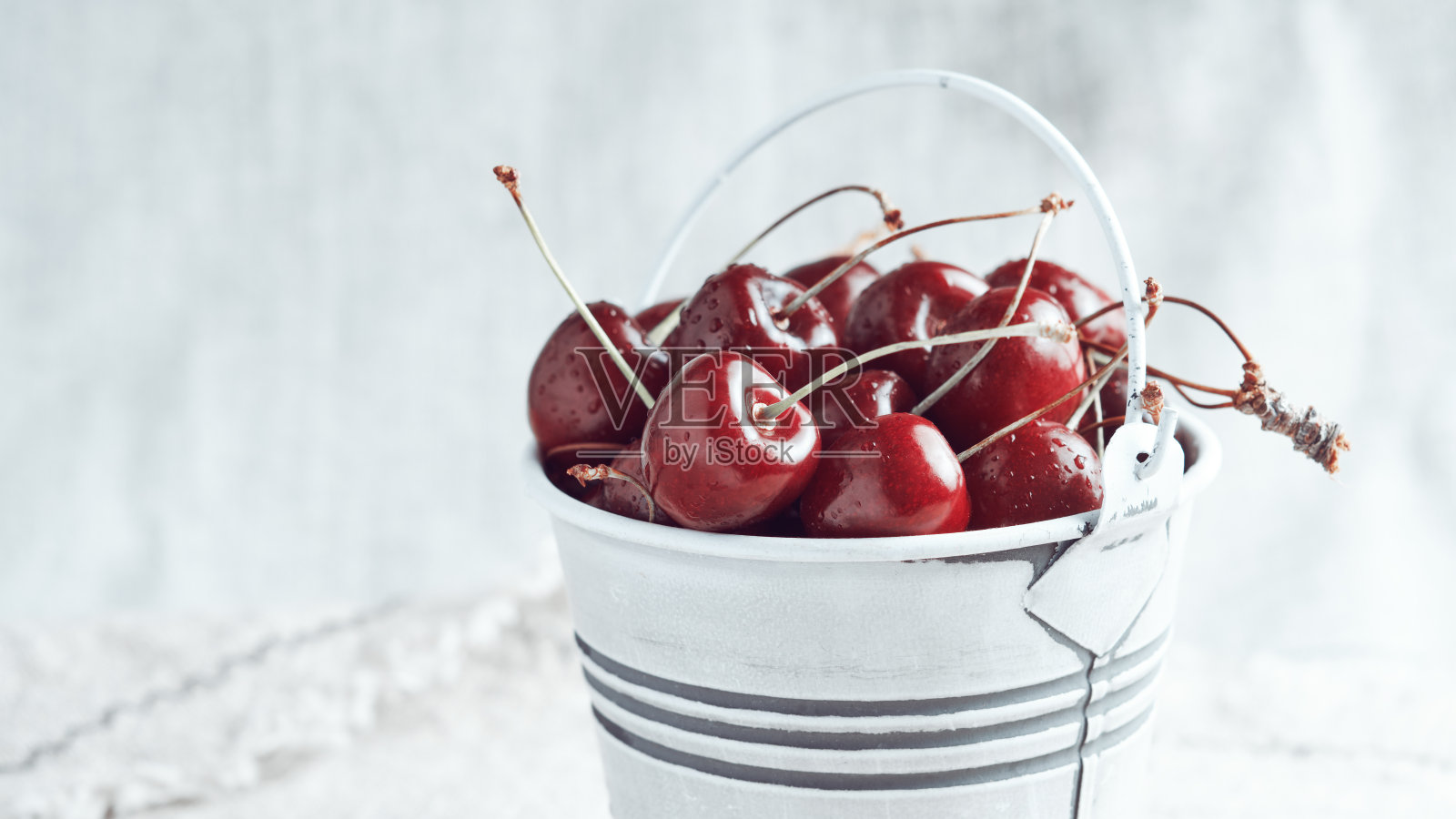 白色的小桶里装满了红色的樱桃，背景很淡。明亮的阳光。照片摄影图片