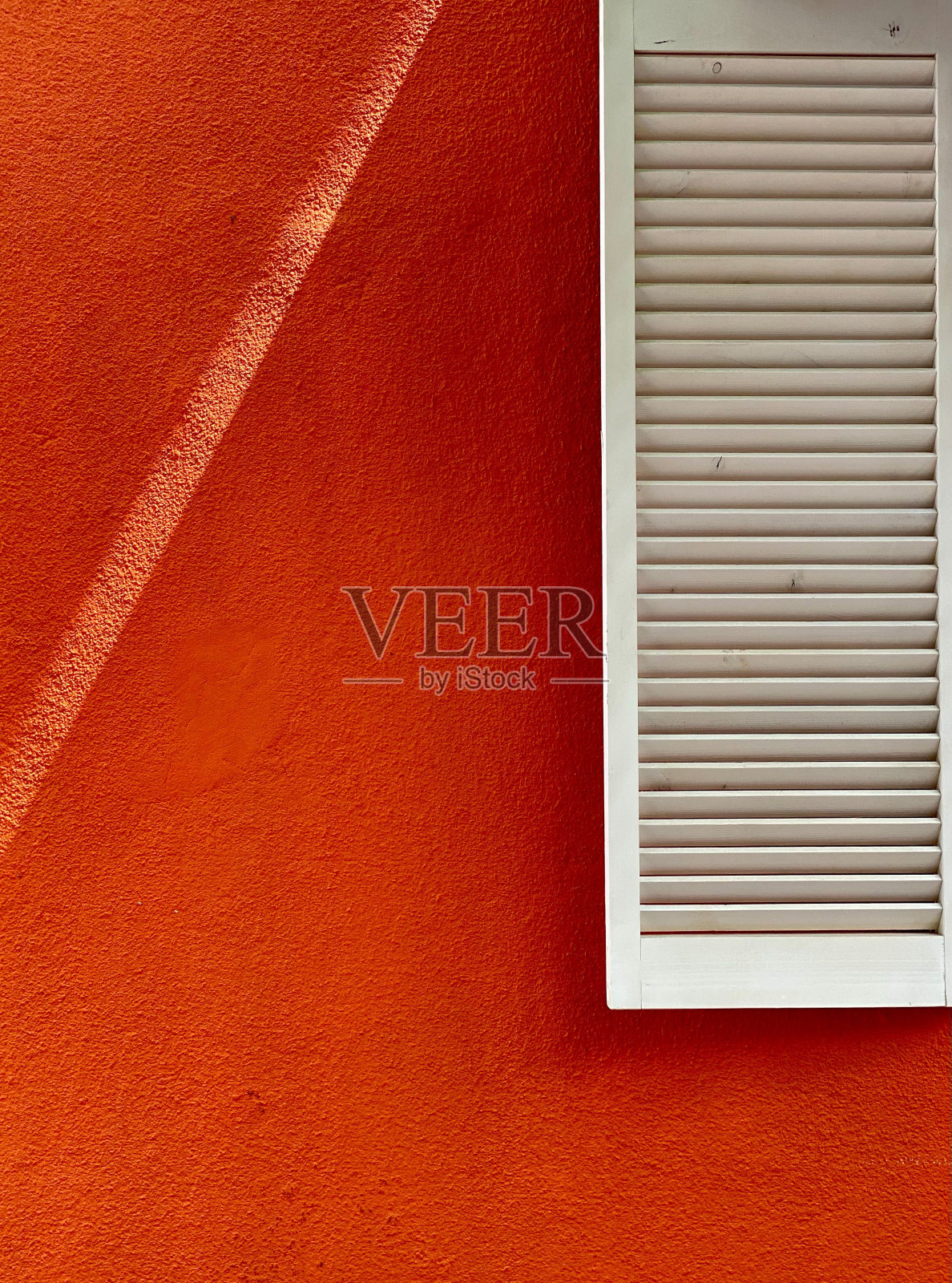 户外鲜红的墙壁上，一扇带百叶窗的白色窗户的垂直镜头照片摄影图片