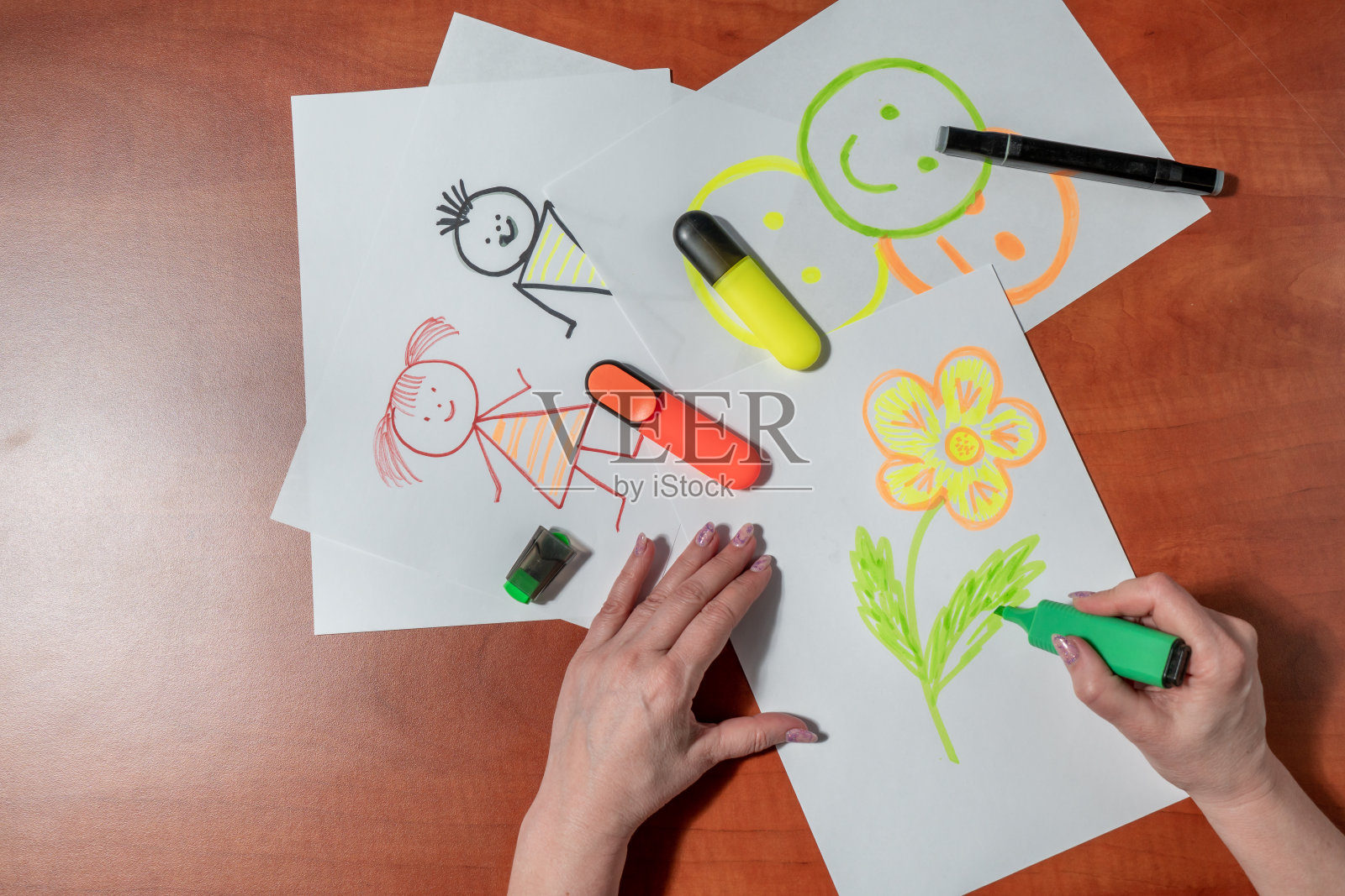 一个女人用毡尖笔在一张白纸上画着小男人。坐在桌子旁。从上面看照片摄影图片