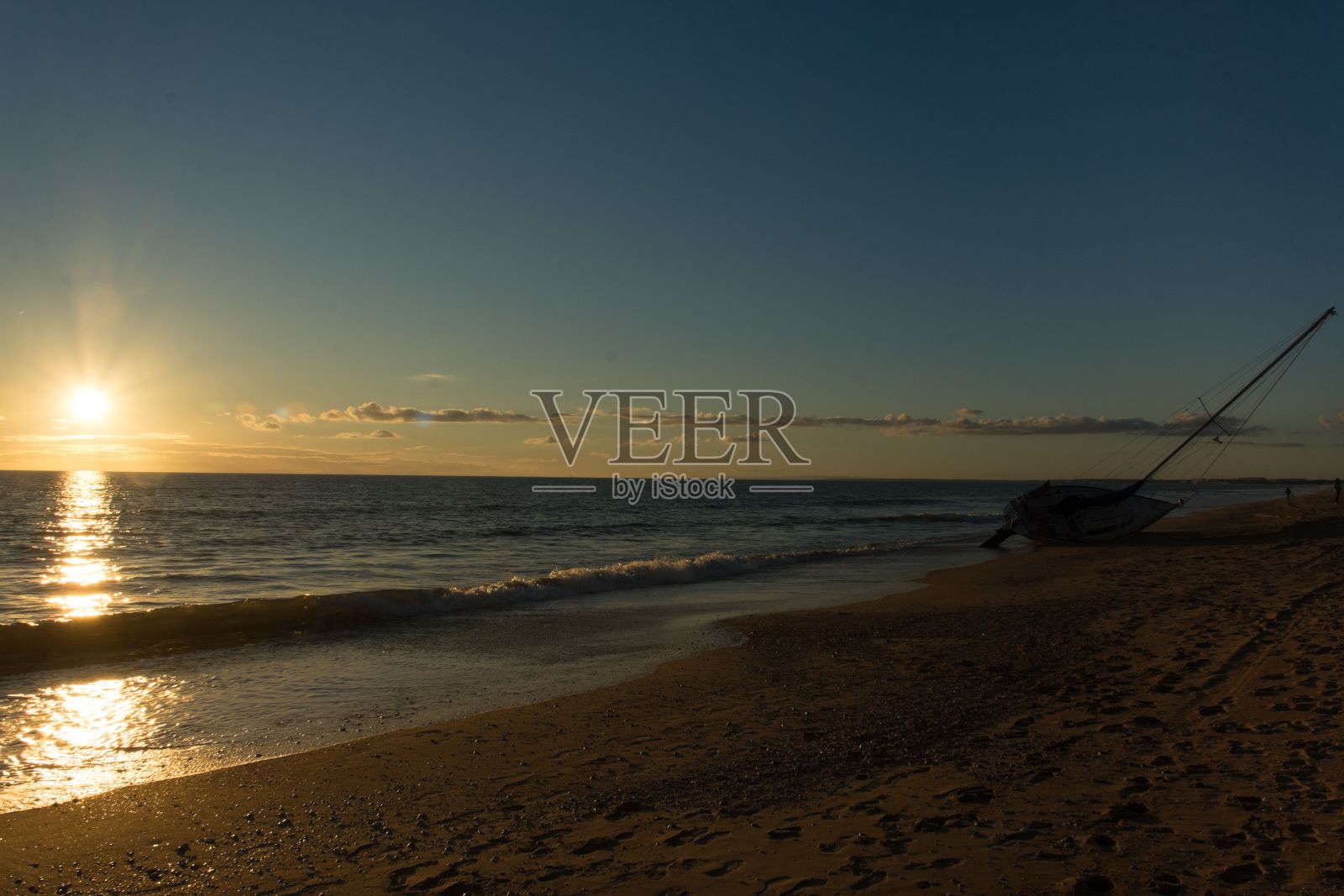 太阳落山时，一艘帆船停在海里照片摄影图片