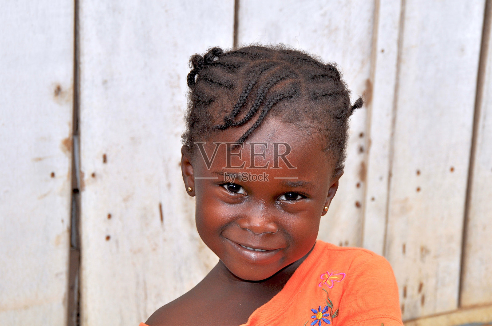 一个微笑的女孩的肖像，她梳着辫子，靠着木栅栏照片摄影图片