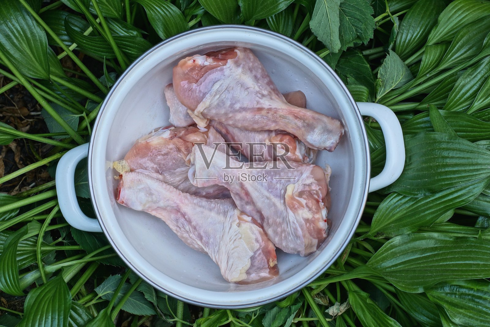 白色平底锅里的一堆生鸡腿上的食物堆在绿叶里照片摄影图片
