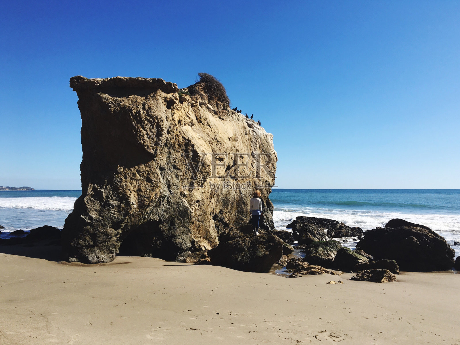 女子站在沙滩上的岩层旁，面对清澈的蓝天照片摄影图片