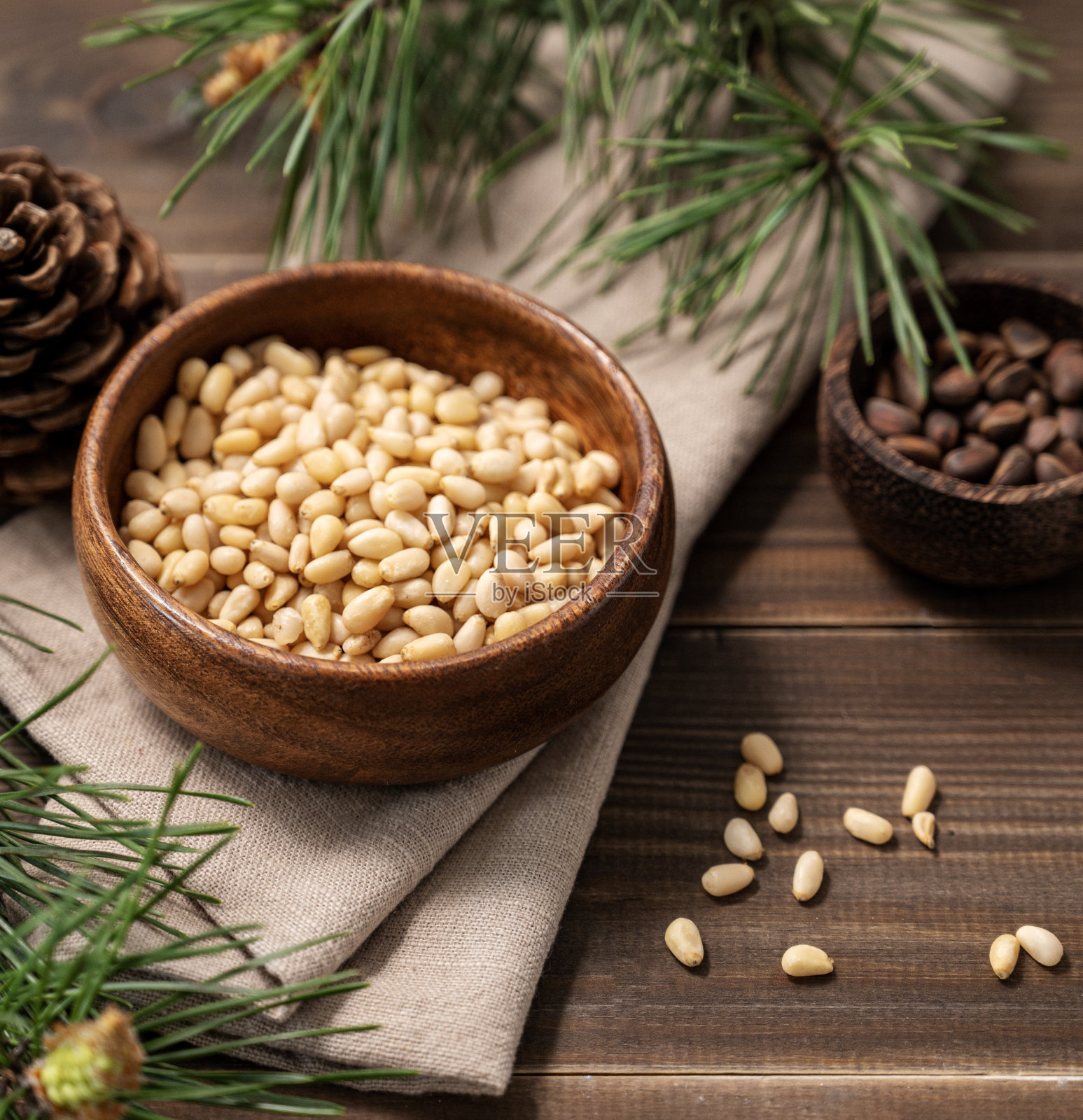碗里放着松子，一把未剥皮的松子放在棕色的木制背景上，旁边是一根松针。照片摄影图片
