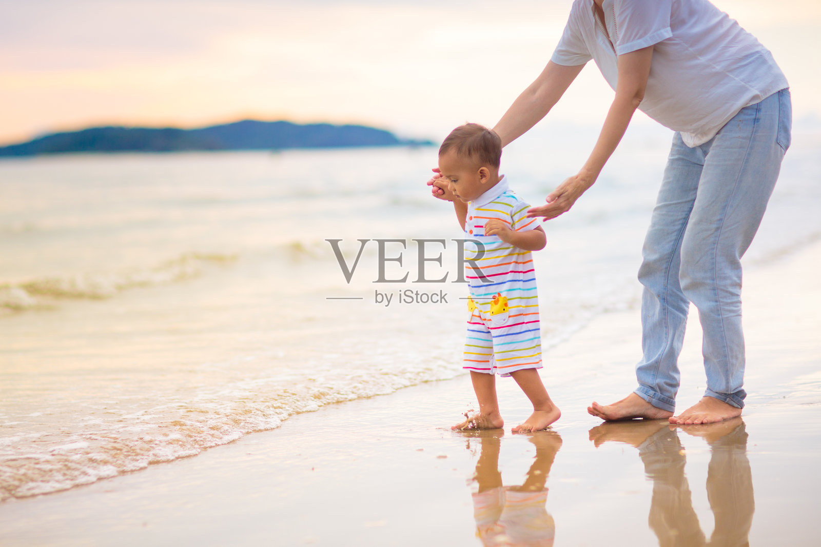 日落时分，母亲和婴儿在热带海滩上。照片摄影图片