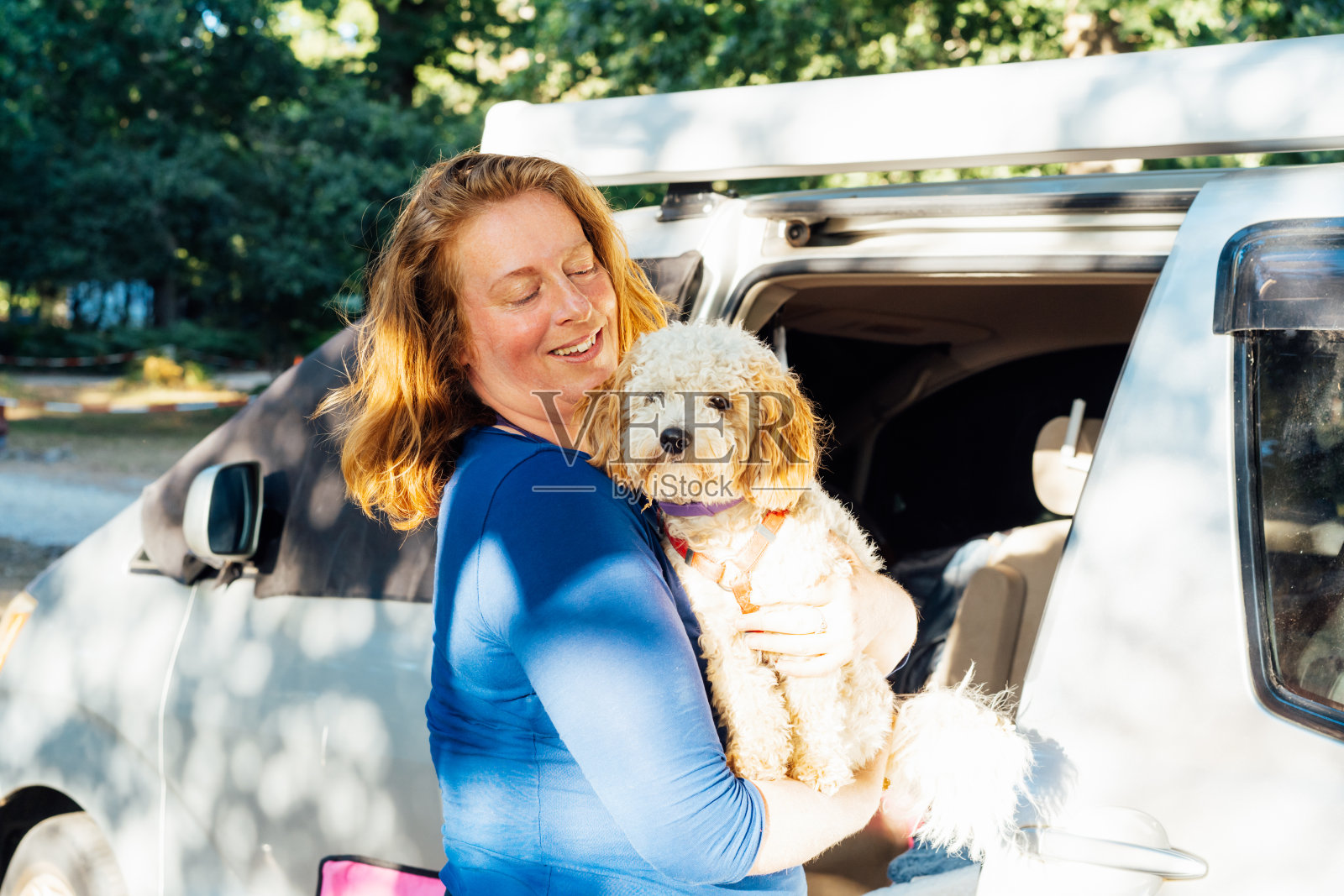 中年妇女在公路旅行中，站在面包车露营车附近，抱着她的小狗狗的照片。最好的朋友。享受自由的生活方式，假期，自由。带宠物旅行。照片摄影图片