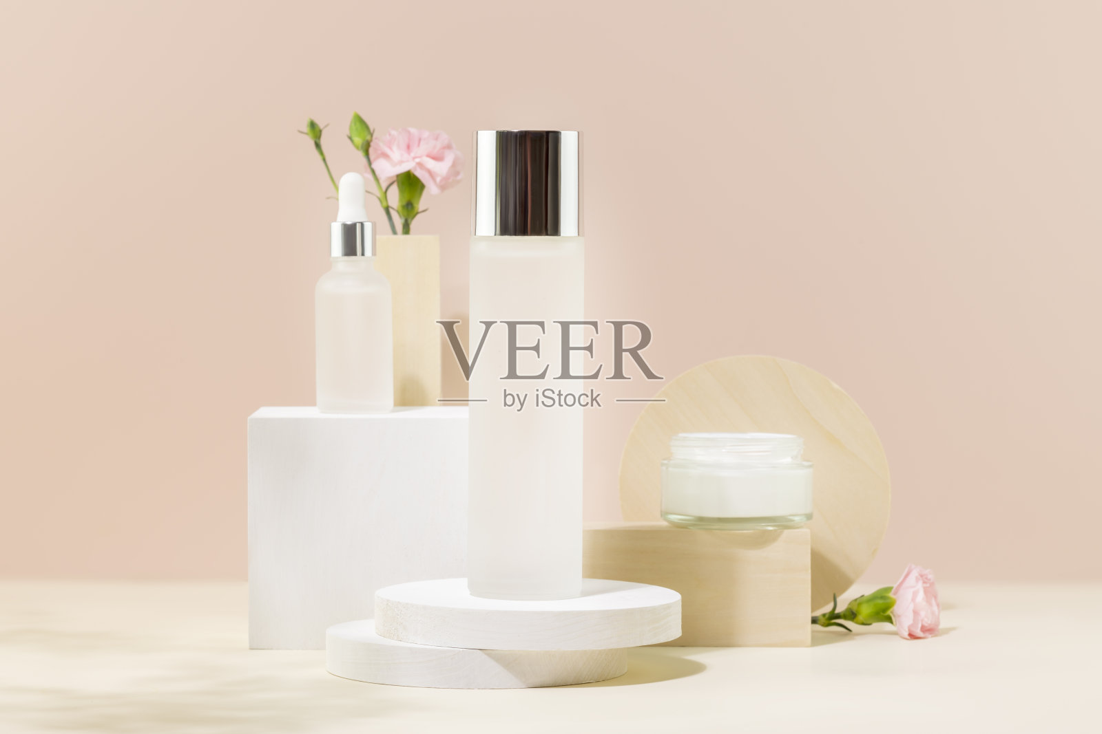 化妆品罐里装着面霜、精华液和化妆水，粉红色的背景上有花照片摄影图片