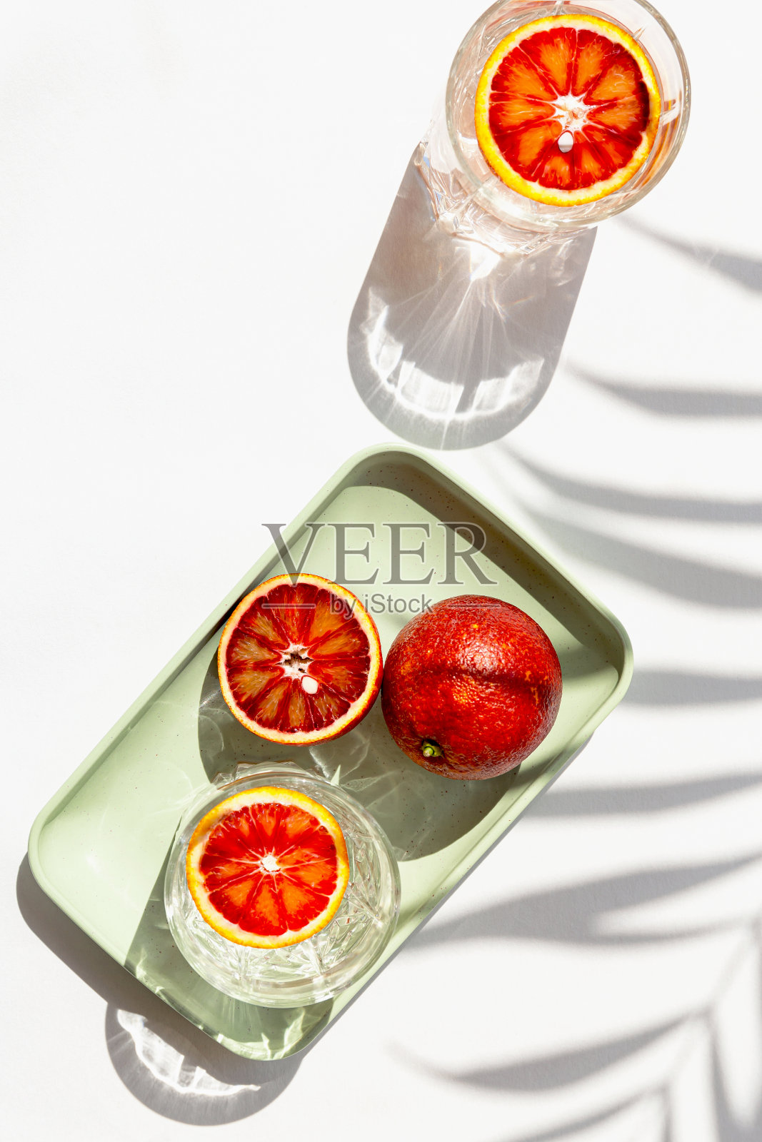 半血橙在托盘和两个杯子鸡尾酒在白色背景与棕榈叶阴影创意构图。夏日茶点和派对概念。最小的风格。俯视图照片摄影图片