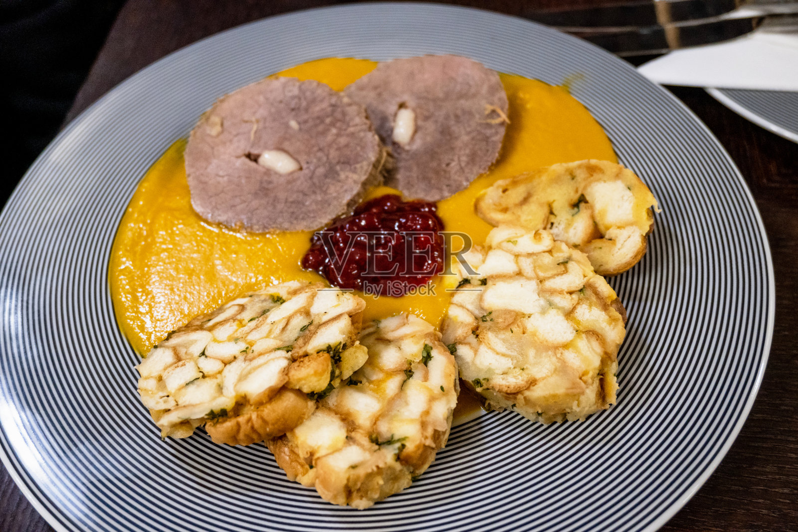 西冷牛排，蔬菜酱，卡尔斯巴德饺子和蔓越莓果酱条纹盘。照片摄影图片