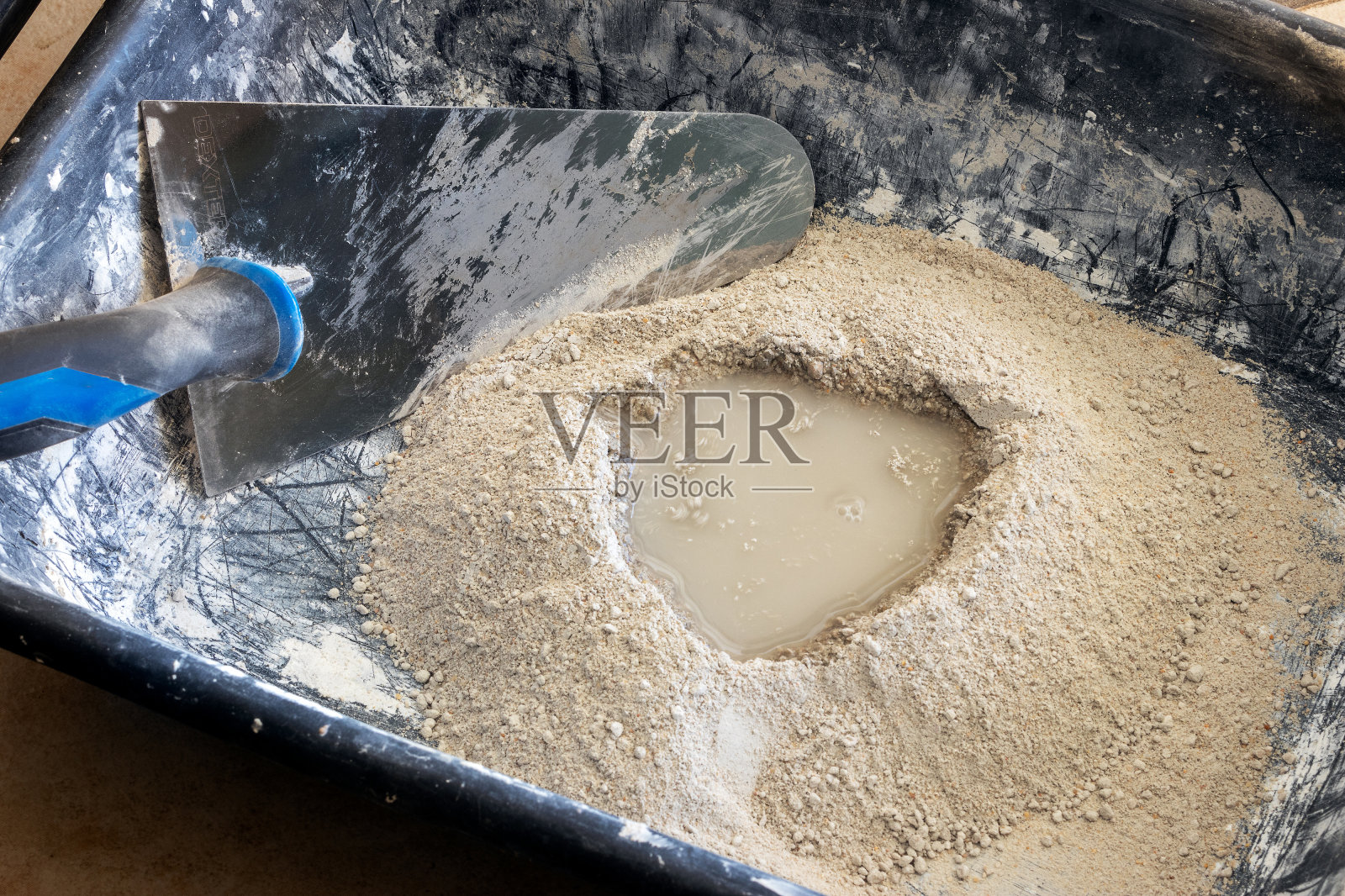 水泥粉加水准备好后，用抹刀在塑料碗中搅拌，进行砂浆的制作过程。照片摄影图片