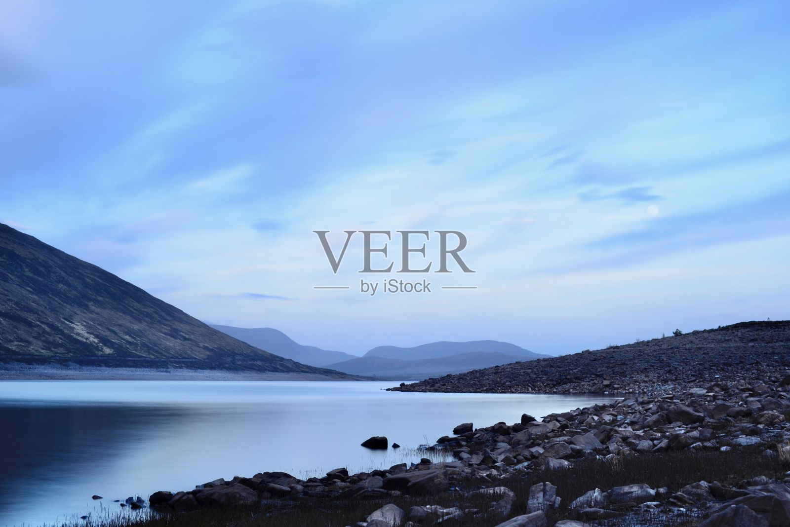 在湖的后面，远处有一座被云覆盖的蓝色山脉照片摄影图片