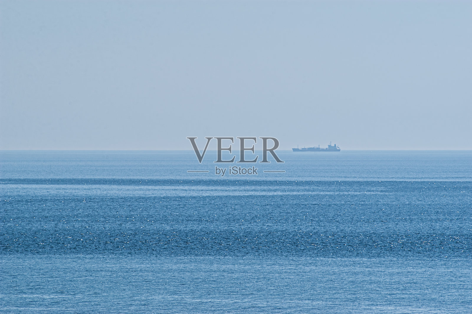 在一个阳光明媚的夏日，一艘货船从地平线上驶过。照片摄影图片