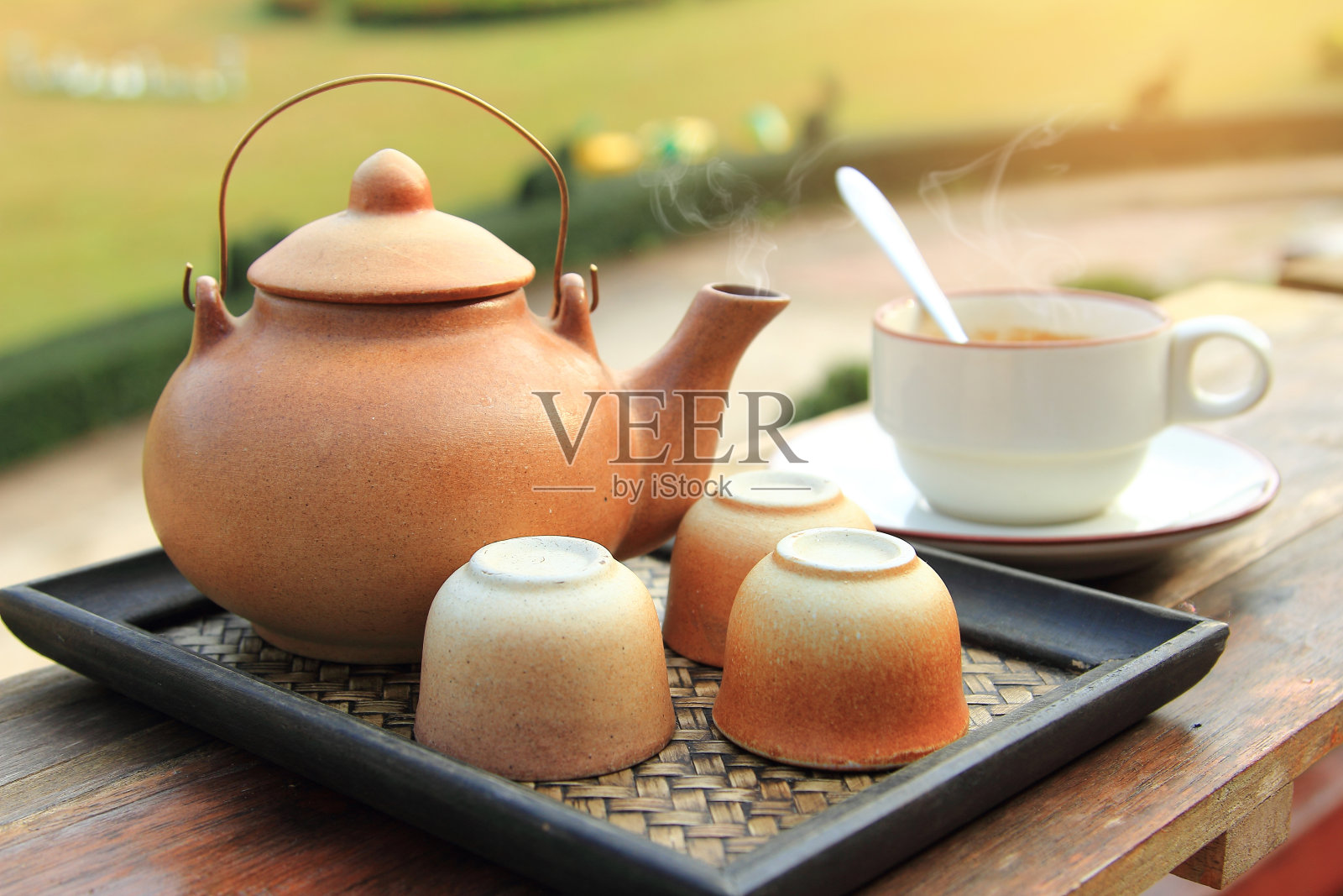 封闭的陶器茶壶，在棕色的杯子里倒入热茶，放在桌子上，供早晨健康饮用照片摄影图片