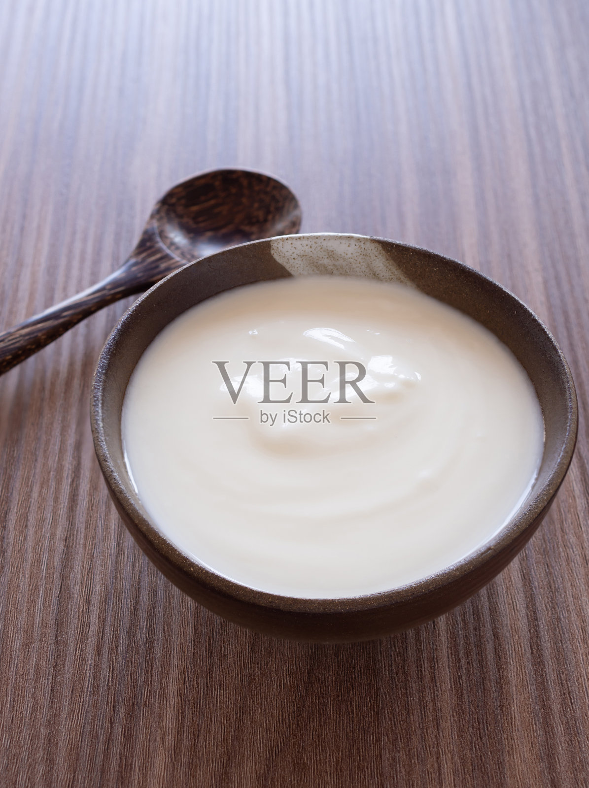 自制希腊酸奶或酸奶油在旧粘土碗与木制背景木勺。食物有助于消化系统。照片摄影图片