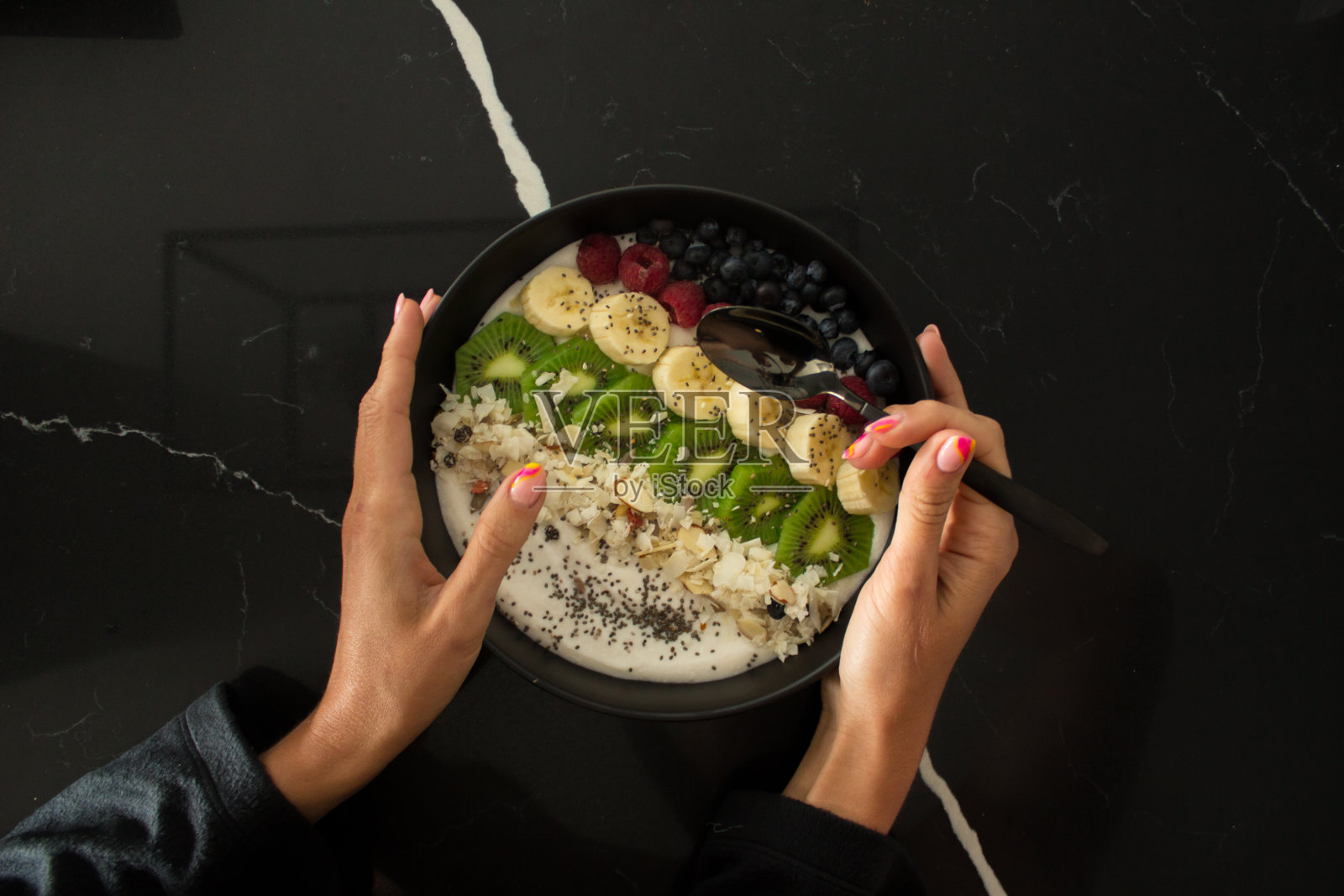 女性手里拿着一盘黑色的燕麦片，里面有新鲜的水果、坚果和奇亚籽，俯视图，健康的快餐。有益健康的早餐。瘦身。食物摆得很漂亮。照片摄影图片