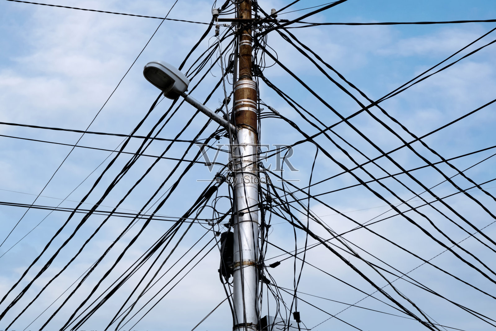 在晴朗的天空下，一根有很多电线和连接线的电线杆。照片摄影图片