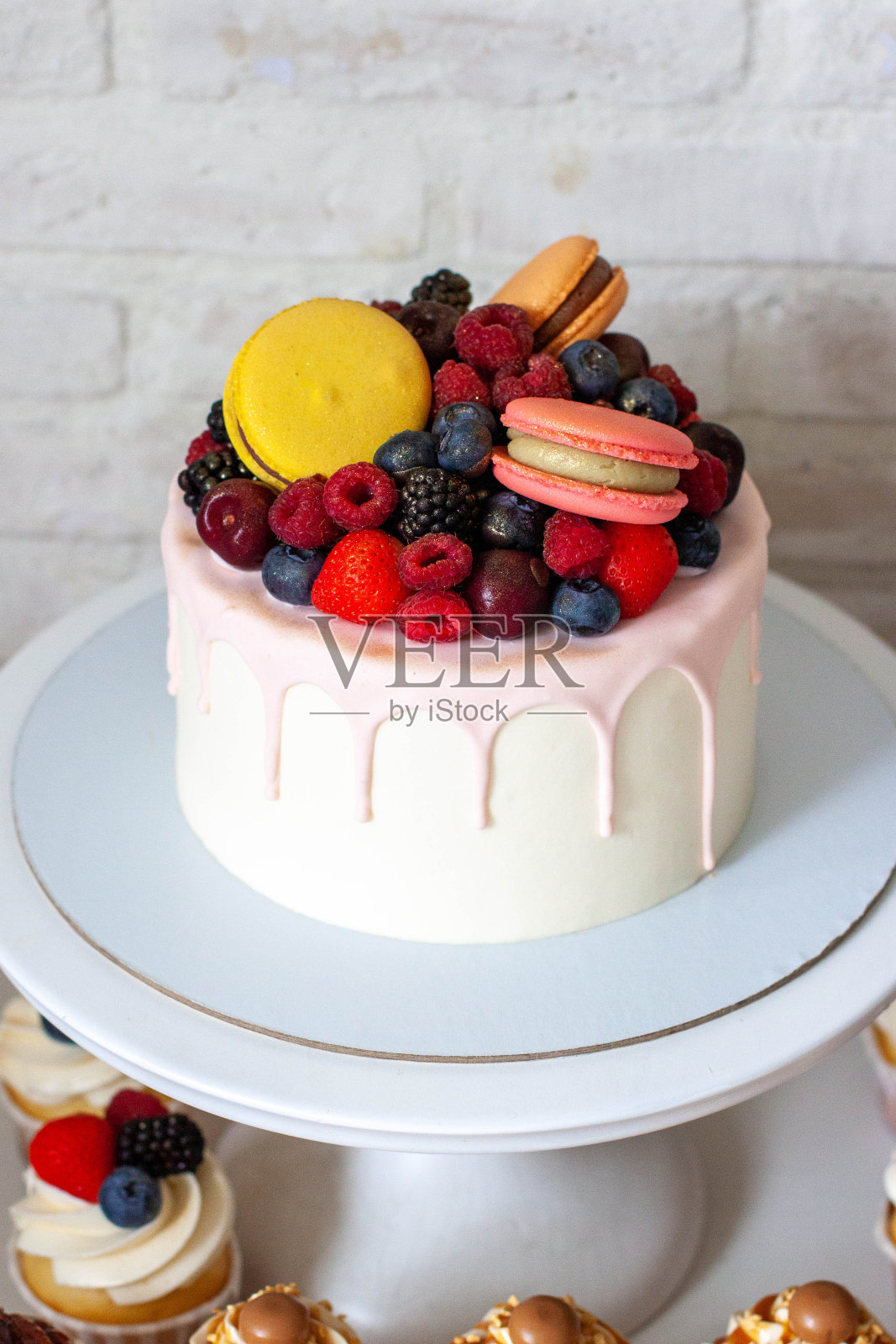白色蛋糕架上装饰着巨大的马卡龙、覆盆子、草莓和蓝莓，上面是融化的粉色巧克力照片摄影图片