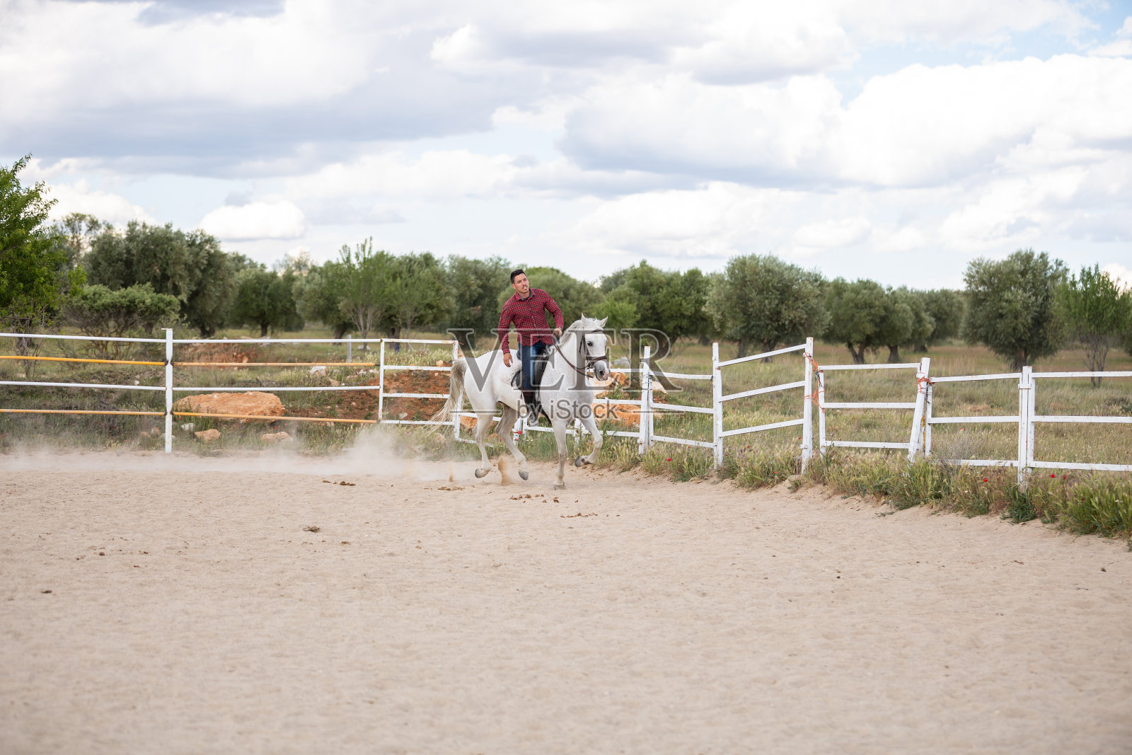 一个穿着便装的年轻人骑着白马在沙地上奔跑照片摄影图片