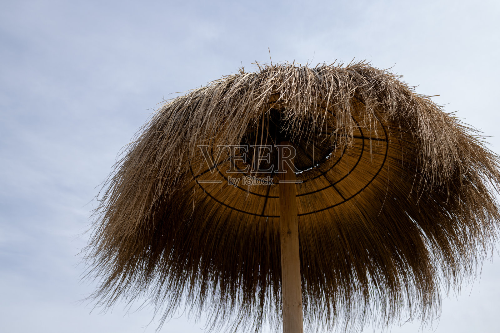 沙滩上的芦苇伞顶，映衬着多云的天空照片摄影图片