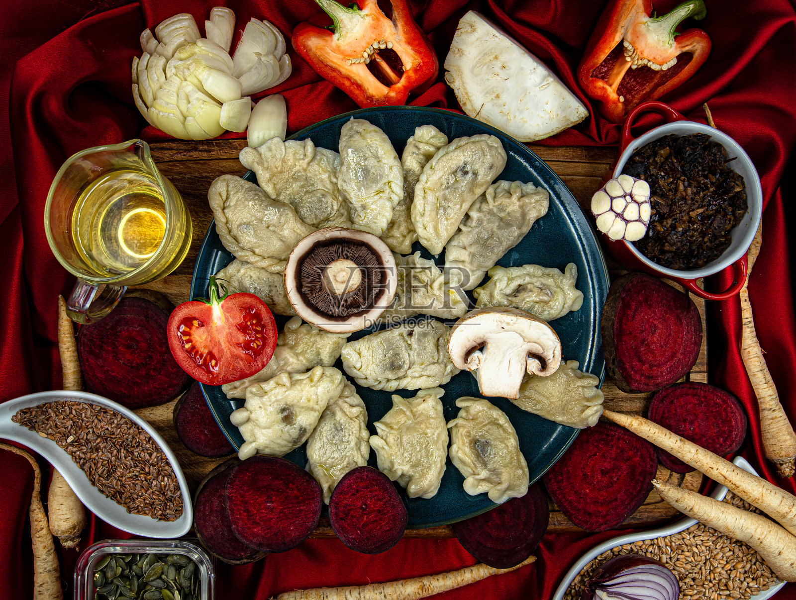 盛满饺子的盘子沿盘子的内边缘排列。木板上的盘子。背景是一块红色的丝绸。平的纬度。从上面俯瞰。照片摄影图片