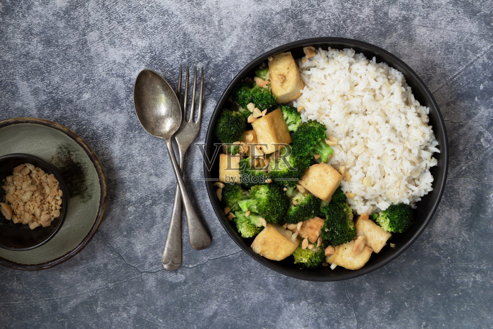 纯素健康食品炒西兰花豆腐花生黑碗糙米石板桌上。照片摄影图片