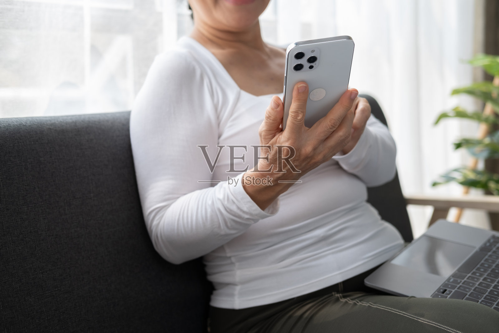 高级女士坐在沙发上看智能手机屏幕的特写。照片摄影图片