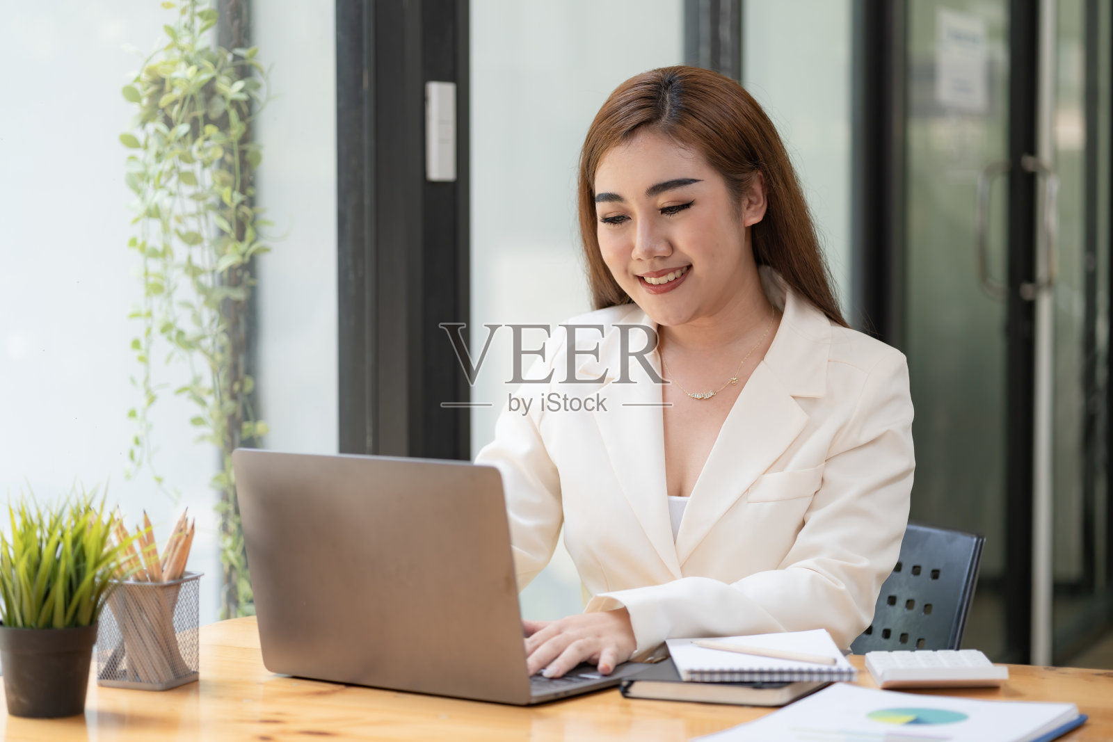 一位亚洲女商人在她的办公桌前用笔记本电脑工作。照片摄影图片