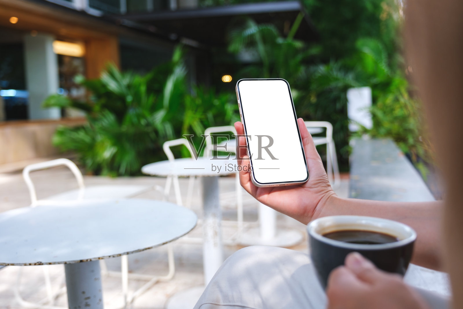 一个女人在户外咖啡馆喝咖啡时手持并使用空白桌面的手机的模拟图像照片摄影图片