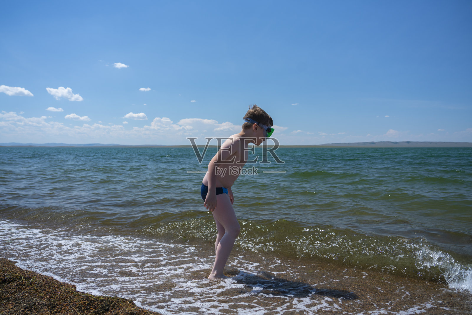 一个戴着潜水面具的7岁男孩站在靠近水的海滩上。照片摄影图片