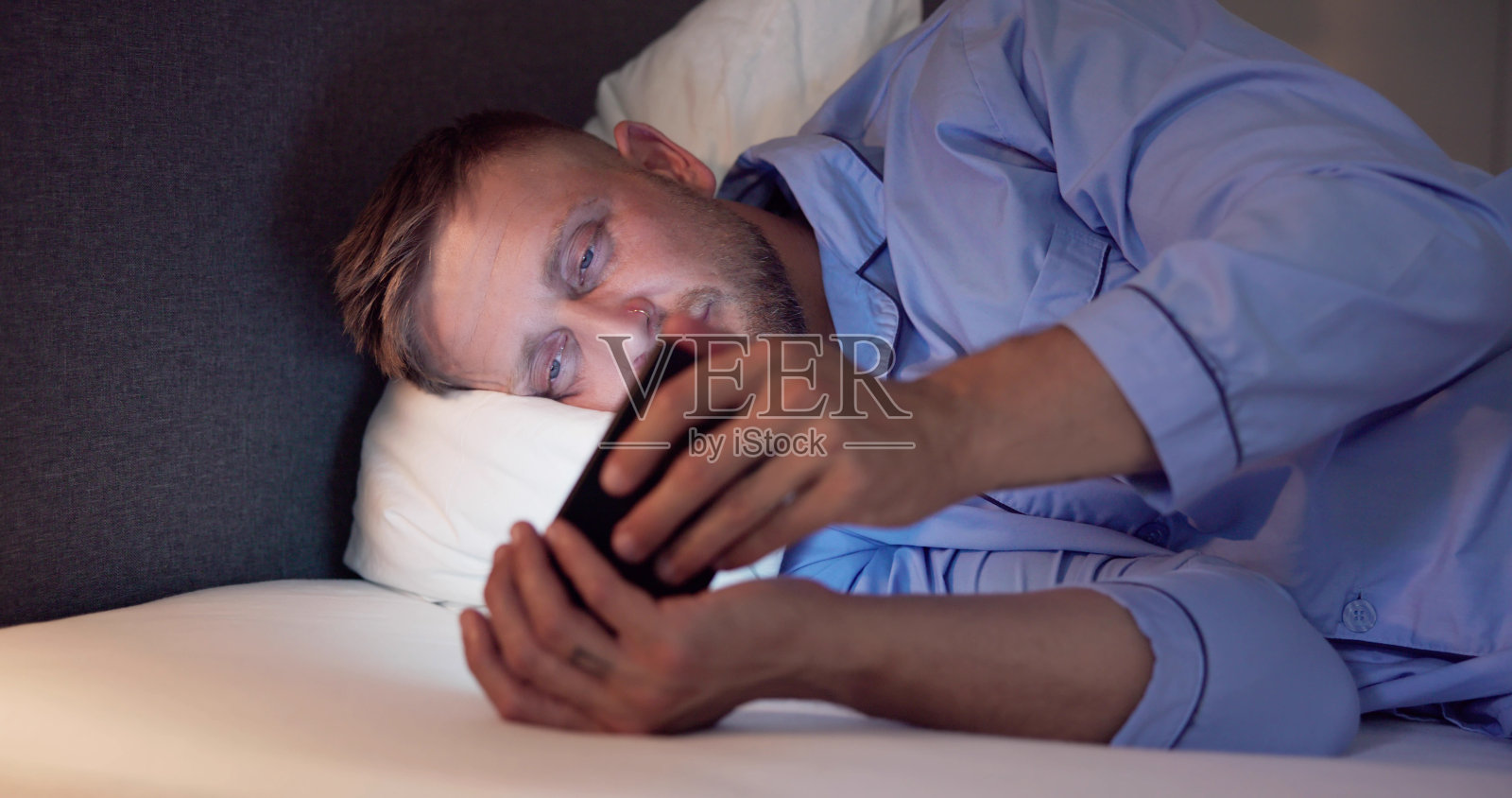 躺在床上玩手机的男人照片摄影图片