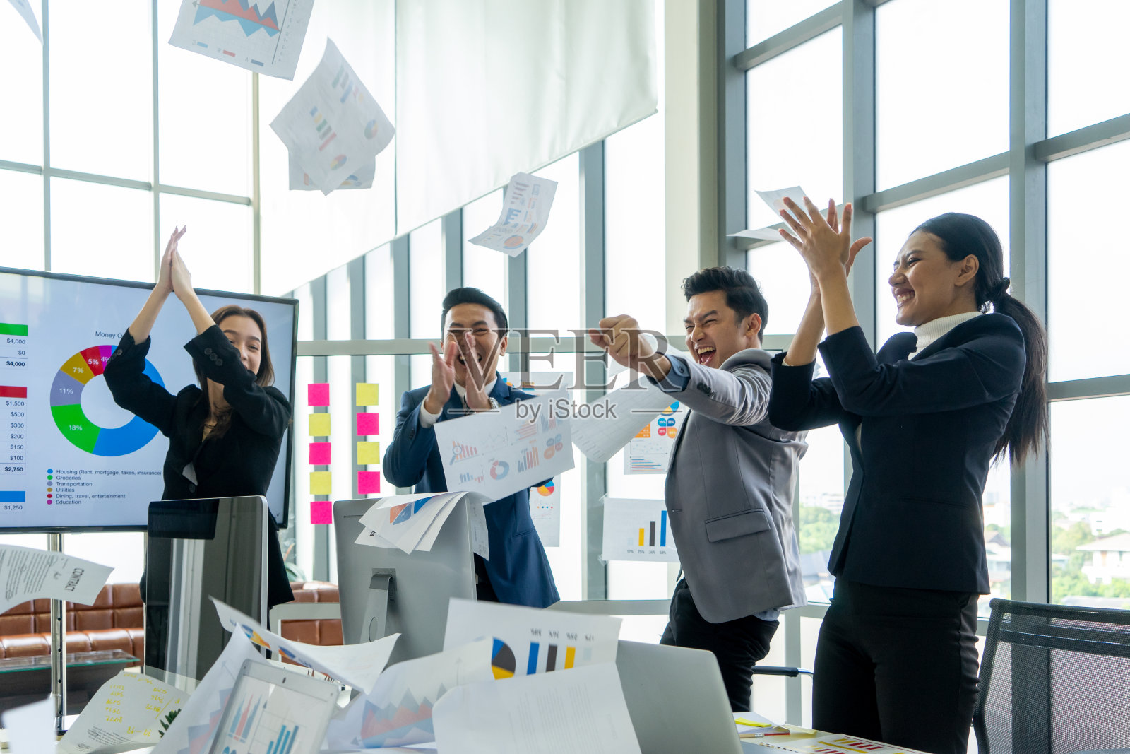 在现代办公室里，一小群商务人士为庆祝成功的项目而扔文书文件照片摄影图片