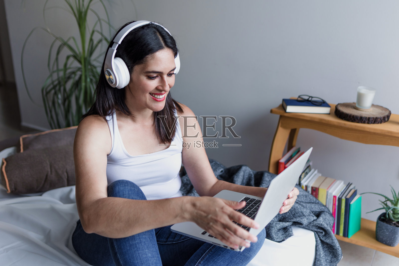 拉丁美洲成年女性在家里坐在沙发上使用笔记本电脑和耳机在墨西哥拉丁美洲，西班牙裔中年女性照片摄影图片