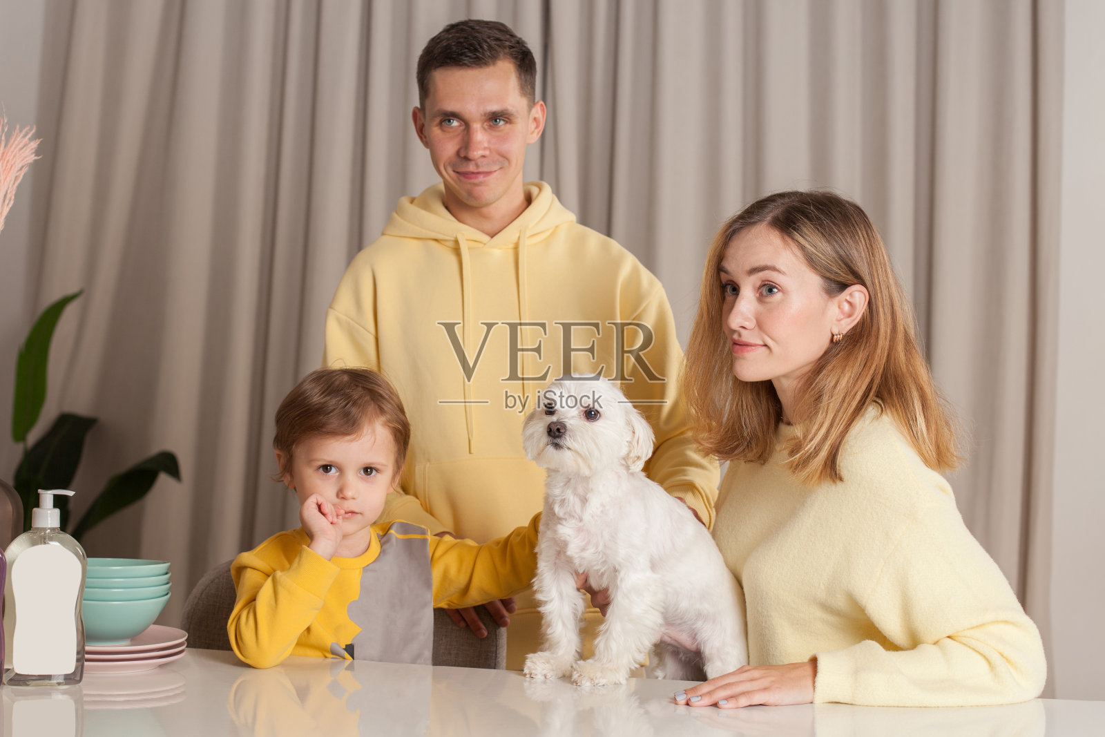 幸福的家庭，穿着黄色毛衣的父母带着孩子和白色的狗，桌子上放着三个抽象的塑料瓶照片摄影图片