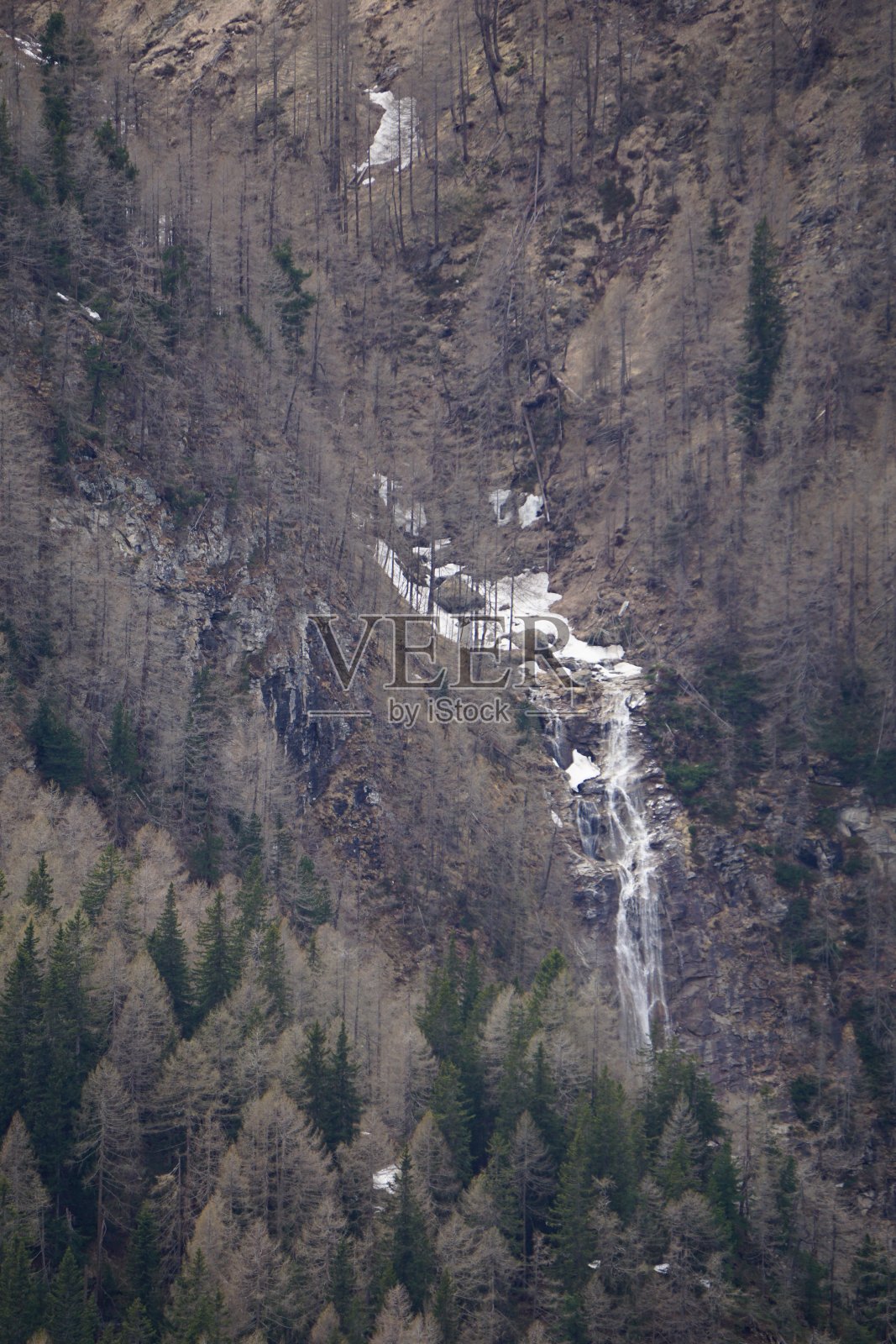 初春阿尔卑斯山的小瀑布。山间小而高的瀑布。棕色的山脉和高高的瀑布。春天阿尔卑斯山的融雪。照片摄影图片