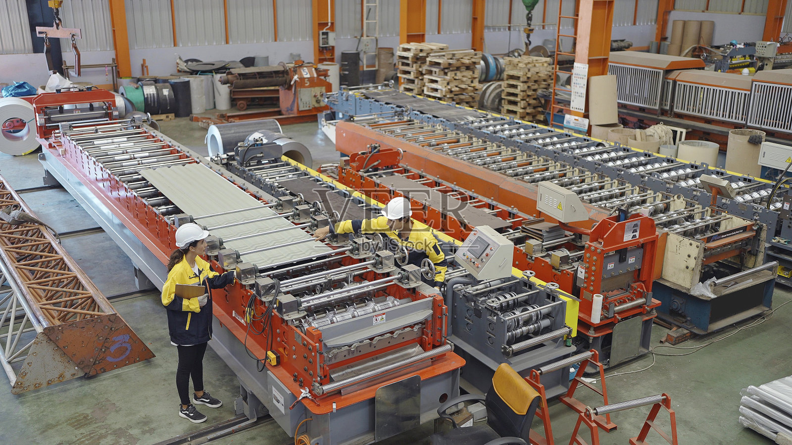 在金属制造厂，男工业工程师向女厂长展示生产金属薄板屋顶的机器流程照片摄影图片