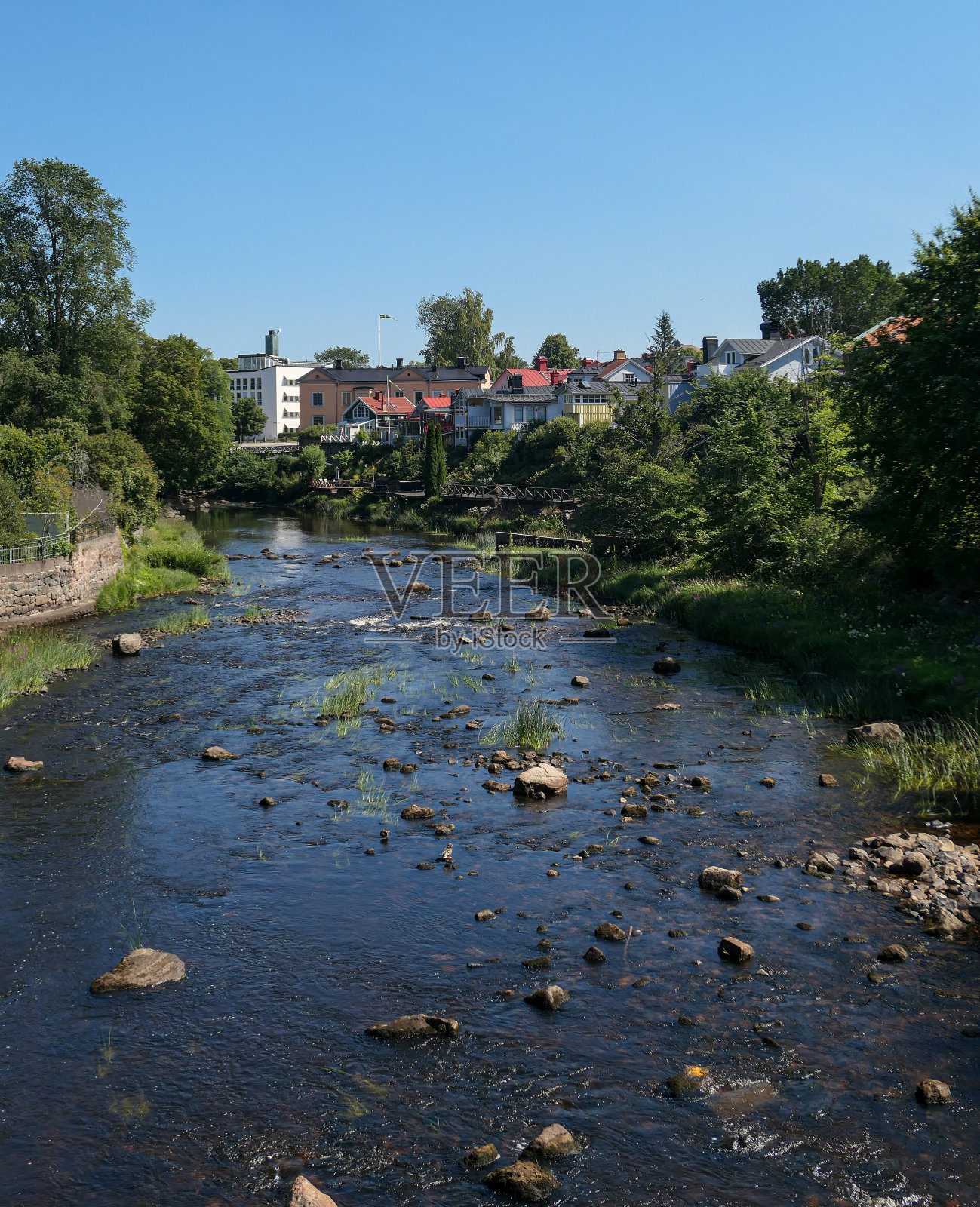 小溪边的树木和建筑物映衬着晴朗的天空照片摄影图片