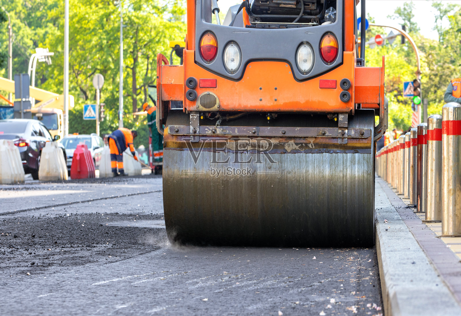 在阳光明媚的日子里压路机的金属滚筒在一段道路上非常精确地压实新