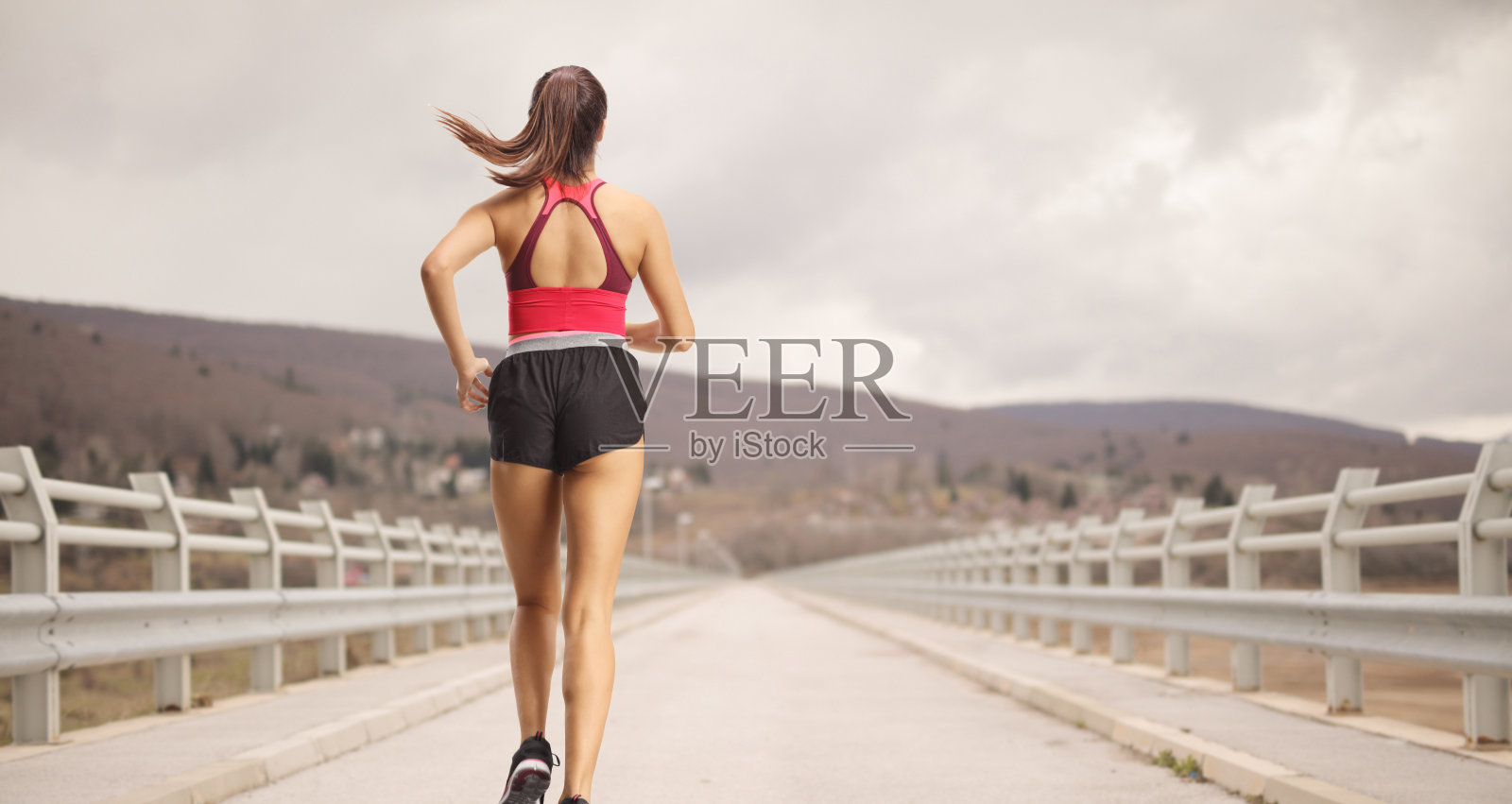 一个穿着运动服的健康女人从桥上跑过的后视图照片摄影图片