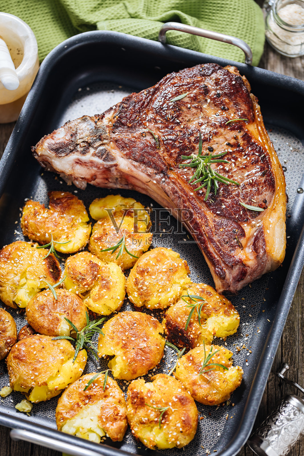 上等牛排配烤土豆，放在金属烤盘里。用迷迭香、胡椒和大蒜调味。多汁美味的肉照片摄影图片